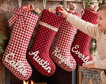 Könnte beinhalten: Vier hängende Weihnachtsstrümpfe in Rot-Weiß-Mustern. Der erste ist kariert mit einer Schleife, die anderen sind gepunktet mit Spitzenbesatz. Jeder Strumpf ist mit einem weiß gestickten Namen versehen.