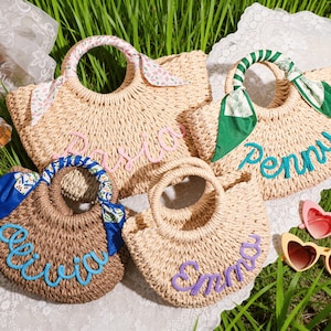 May include: Four woven straw handbags with round handles, each featuring a personalized name in cursive script. The bags are decorated with colorful fabric ribbons tied to the handles, displaying the names Pasia, Penny, Olivia, and Emma.