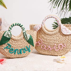 May include: Two woven straw handbags with rounded handles. The left bag features a green scarf wrapped around the handle and the name Penny in teal script. The right bag has a floral scarf and the name Basia in pink script on the front.
