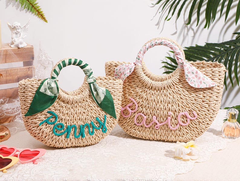 May include: Two woven straw handbags with rounded handles. The left bag features a green scarf wrapped around the handle and the name Penny in teal script. The right bag has a floral scarf and the name Basia in pink script on the front.