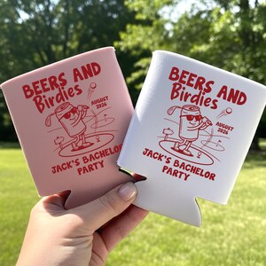 May include: Two beverage insulators, one pink and one white, with the text "BEERS AND Birdies" and "JACK'S BACHELOR PARTY" in red. Each features a cartoon can playing golf, with the date "AUGUST 2026".