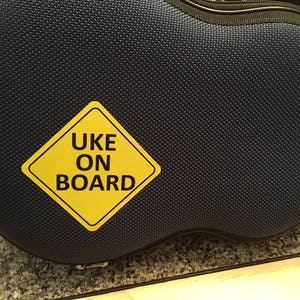 May include: A blue ukulele case with a yellow warning sign that says "UKE ON BOARD".