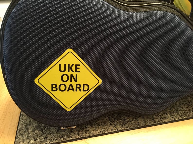 May include: A blue ukulele case with a yellow warning sign that says "UKE ON BOARD".