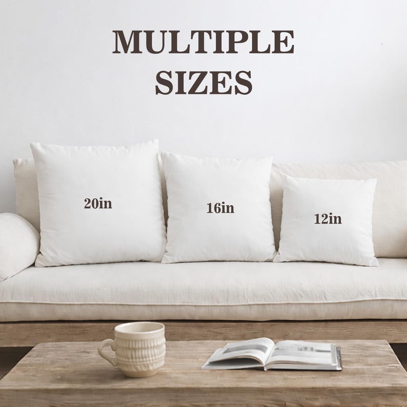 May include: Three white square pillows of varying sizes, 20in, 16in, and 12in, are arranged on a cream-colored sofa. The text "MULTIPLE SIZES" is above the pillows. A wooden coffee table in front holds a mug and an open book.