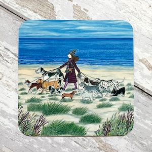 May include: A woman in a purple coat and a scarf walks along a sandy beach with a group of dogs on leads. The dogs are a variety of breeds and colours, including a Dalmatian, a dachshund, and a terrier. The sea is in the background.