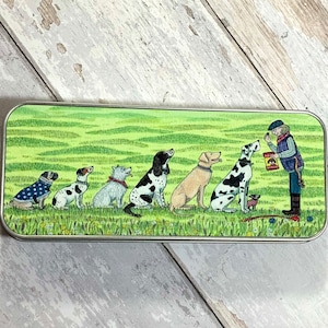 May include: A metal tin with a green and brown landscape scene featuring a man giving treats to a line of dogs. The dogs are a pug, a terrier, a white dog, a black and white dog, a golden retriever, and a dalmatian. The text on the treat bag says "Dog Snacks".