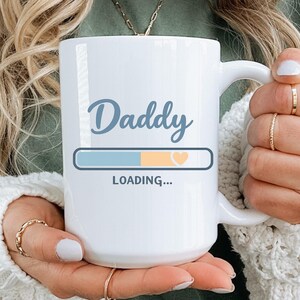 Peut inclure: Une tasse en céramique blanche avec une anse noire et le texte "But First, Coffee" en noir, en gras. La tasse est posée sur une surface en bois. La tasse mesure environ 10 cm de haut.