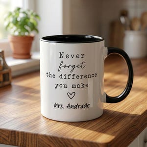 May include: A white ceramic mug with a black interior and handle. The front features black text that reads: Never forget the difference you make, followed by a small heart icon and the name Mrs. Andrade in a script font.