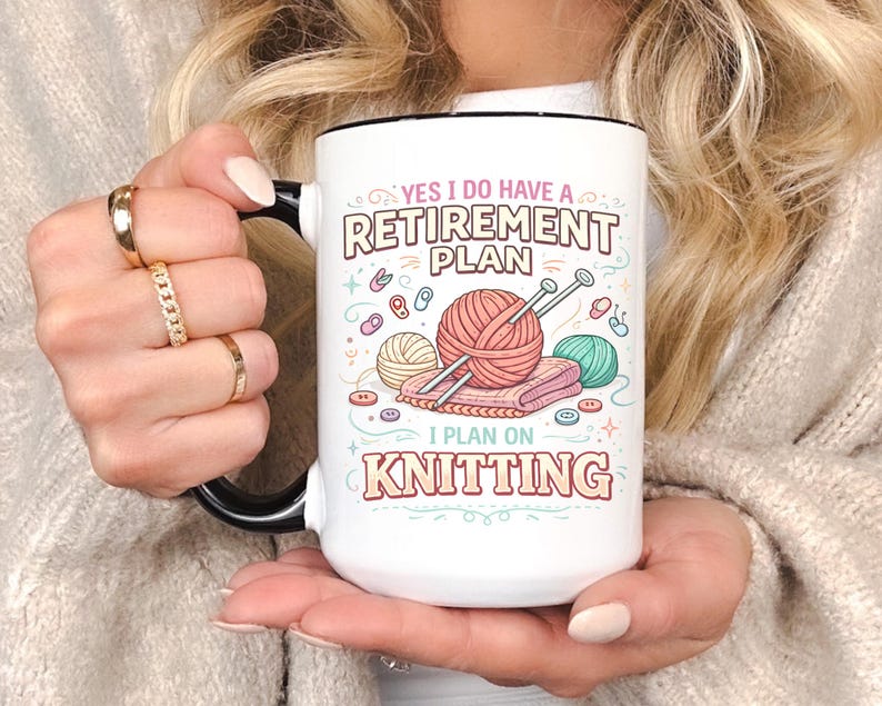 Op de afbeelding: Witte keramische mok met een zwarte handgreep en rand, met de tekst "YES I DO HAVE A RETIREMENT PLAN I PLAN ON KNITTING". Het ontwerp bevat illustraties van garen, breinaalden en knopen in pastelkleuren.