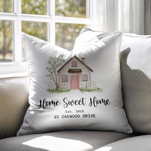 Könnte beinhalten: Weißes Zierkissen mit einer Aquarellillustration eines Hauses, Baumes und Zauns. Der Text "Home Sweet Home" ist in Schreibschrift geschrieben, darunter "Est. 2018" und "45 OAKWOOD DRIVE".