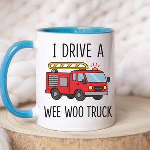 May include: White ceramic mug with a blue handle and interior. The mug features a red cartoon fire truck with a yellow ladder and the text "I DRIVE A WEE WOO TRUCK" in black.
