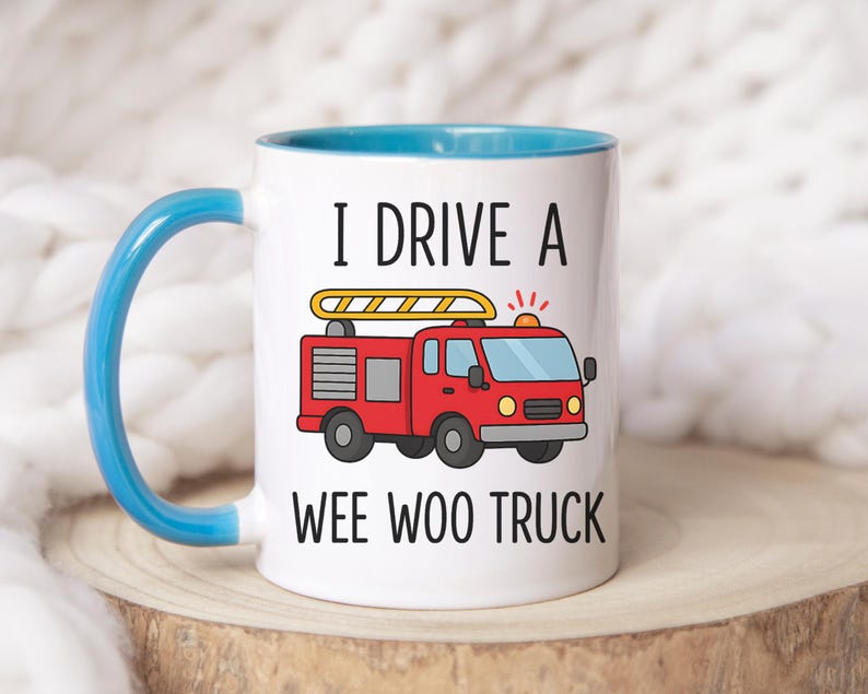 May include: White ceramic mug with a blue handle and interior. The mug features a red cartoon fire truck with a yellow ladder and the text "I DRIVE A WEE WOO TRUCK" in black.