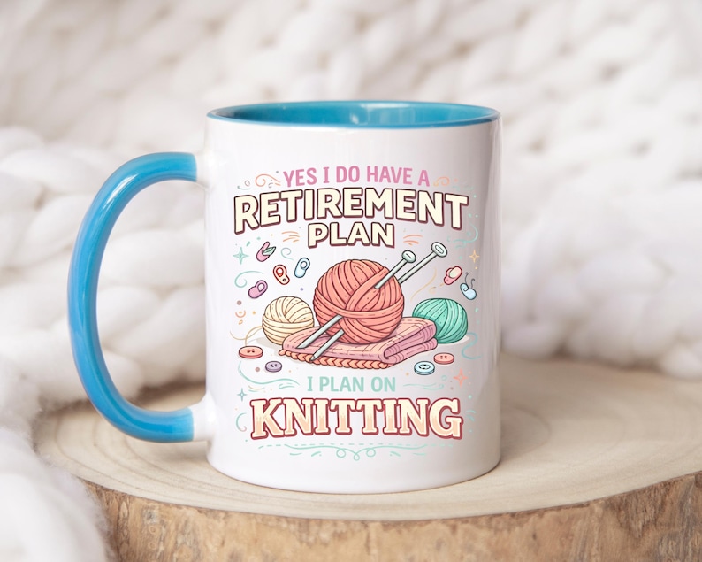 Op de afbeelding: Witte keramische mok met een blauwe handgreep en binnenkant. De mok heeft de tekst "YES I DO HAVE A RETIREMENT PLAN I PLAN ON KNITTING" met illustraties van garen, breinaalden en knopen. De mok staat op een houten oppervlak.