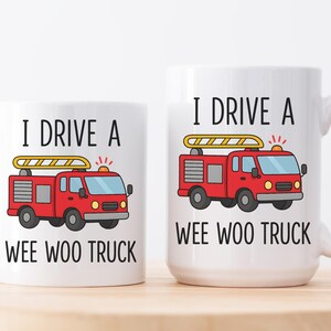 May include: Two white ceramic mugs with the text "I DRIVE A WEE WOO TRUCK" and a cartoon fire truck design. The fire truck is red with a yellow ladder and flashing lights. One mug is smaller than the other.
