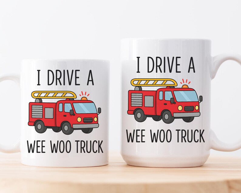 May include: Two white ceramic mugs with the text "I DRIVE A WEE WOO TRUCK" and a cartoon fire truck design. The fire truck is red with a yellow ladder and flashing lights. One mug is smaller than the other.