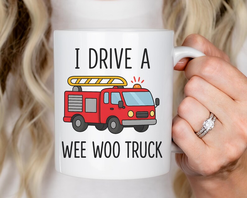 May include: White ceramic mug with the text "I DRIVE A WEE WOO TRUCK" and a cartoon illustration of a red fire truck. The fire truck has a yellow ladder and flashing lights.