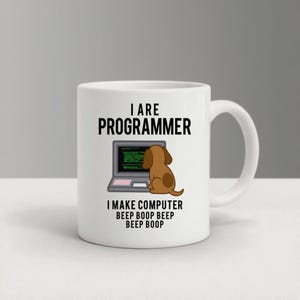 May include: White ceramic mug with the text "I ARE PROGRAMMER" above a cartoon image of a laptop and a brown dog. Below the image is the text "I MAKE COMPUTER BEEP BOOP BEEP BEEP BOOP".