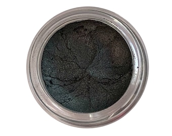 May include: A jar of dark green eyeshadow with a metallic sheen. The eyeshadow is in a clear, round container. The product is on a white background.