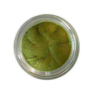 May include: A jar of shimmering, olive-green eyeshadow. The makeup is contained in a clear, round jar with a silver lid. The eyeshadow has a metallic sheen and a smooth, creamy texture.