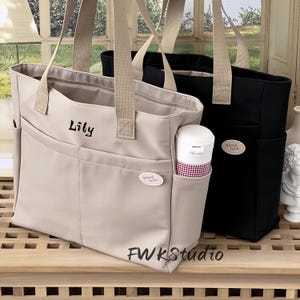 Peut inclure: Deux sacs fourre-tout, un beige et un noir, avec des anses beiges. Le sac beige porte le nom "Lily" imprimé et un petit écusson "good luck!". Une bouteille d'eau blanche est dans la poche latérale. Le texte "FWKStudio" est en bas.