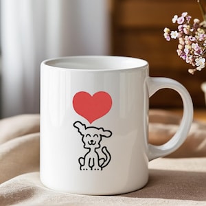 Puede incluir: Taza de cerámica blanca con un dibujo lineal negro de un perro y un corazón rojo encima. La taza tiene un asa curvada. El diseño es sencillo y encantador. La taza está sobre un fondo neutro.