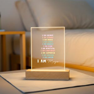 May include: A rectangular LED night light with a wooden base. The light displays the text "I AM UNIQUE, I AM STRONG, I AM BRAVE, I AM SMART, I AM HONEST, I AM KIND, I AM BEAUTIFUL, I AM CONFIDENT, I AM SUPPORTED, I AM ENOUGH, I AM LOVED" and "I AM Maya" in a colorful font.
