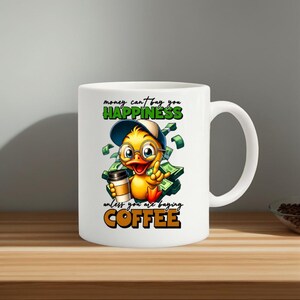 Op de afbeelding: Witte keramische koffiemok met een cartoon eend met een bril en een hoed, die een koffiekopje vasthoudt. De mok heeft de tekst "money can't buy you happiness unless you are buying COFFEE".