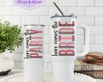 May include: White tumblers with the text "here comes the PARTY" and "here comes the BRIDE" in pink and leopard print. One tumbler is 20 oz, the other is 40 oz. Both have lids and straws. The tumblers are on a white surface.