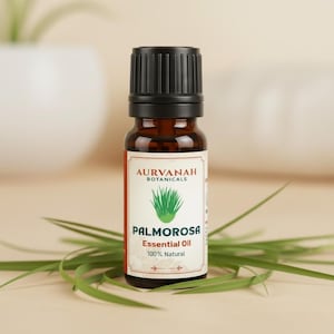 Puede incluir: Una botella de vidrio marrón de Aceite Esencial de Palmarosa de Aurvanah Botanicals, con tapa negra. La etiqueta presenta una ilustración de planta verde y las palabras "Palmarosa Essential Oil 100% Natural". La botella descansa sobre hojas verdes.