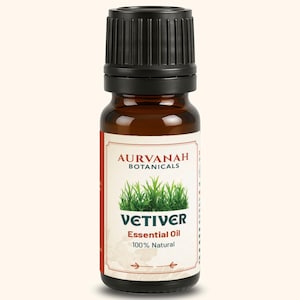 Puede incluir: Una botella de vidrio marrón con tapa negra, etiquetada como "AURVANAH BOTANICALS". La etiqueta presenta imágenes de hierba verde y la palabra "VETIVER" en letras grandes, con "Essential Oil 100% Natural" debajo.