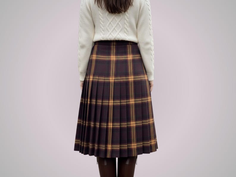 May include: A pleated, knee-length skirt in a brown and yellow plaid pattern. The skirt is paired with a cream-colored cable-knit sweater. The overall style is classic and preppy.