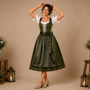 Könnte beinhalten: Eine Frau in einem traditionellen grünen Dirndlkleid mit weißer Bluse und schwarzer Schürze. Das Kleid hat ein eng anliegendes Mieder mit Schnürung und einen weiten Rock. Sie trägt beige Pumps und hat die Hände über dem Kopf.
