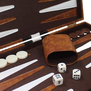 May include: A close-up of a backgammon set, featuring a brown leather case with white and brown playing pieces. Three dice and a leather dice cup are also visible, ready for a game.