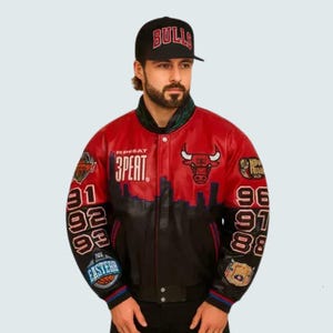 May include: Red and black leather jacket with the Chicago Bulls logo and the word "3PEAT". The jacket has the numbers 91, 92, 93, 96, 97, and 98 on the sleeves. A black baseball cap with "BULLS" is also visible.