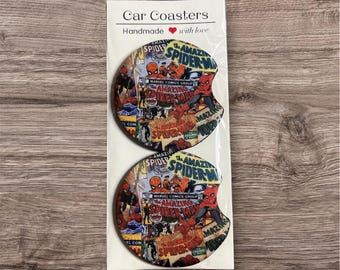 May include: Two car coasters featuring a colorful collage of Spider-Man comic book covers. The coasters are round with a curved notch and are packaged in a white card that reads "Car Coasters, Handmade with love."