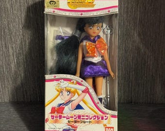 May include: A Sailor Moon mini-collection doll in its original box. The doll has black hair, a purple skirt, and an orange bow. The box features Japanese text and a cartoon illustration of Sailor Moon.
