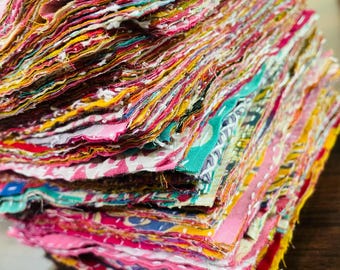 May include: A stack of colorful fabric scraps in various patterns and hues, including pink, yellow, green, and red. The edges of the fabric are visible, creating a textured appearance. The image showcases a collection of textile remnants, ideal for crafting or quilting projects.