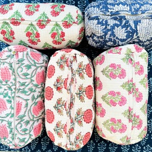 Op de afbeelding: Vijf rechthoekige gewatteerde stoffen etuis met ritssluitingen. Vier etuis hebben een crèmekleurige achtergrond met roze en groene bloemenprints, terwijl één etui een donkerblauwe achtergrond heeft met een witte bloemenprint.