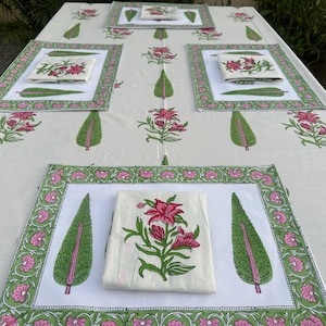 Op de afbeelding: Een witte tafelkleed met bijpassende placemats en servetten, allemaal met een bloemmotief. Het ontwerp bevat roze bloemen en groene bladeren. De placemats en het tafelkleed hebben een groene en roze rand.