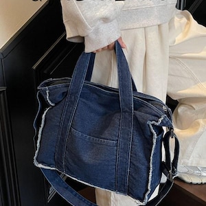 May include: A dark blue denim tote bag with a front pocket and a long, adjustable shoulder strap. The bag has two short handles and a zipper closure. The edges of the bag have a frayed design. The text "Gifts Best Ideas" is visible in the upper left corner.