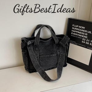 May include: A black denim tote bag with a shoulder strap and two handles. The bag has a front pocket and side pockets. The text "Gifts Best Ideas" is above the bag. A framed sign with text is to the right.