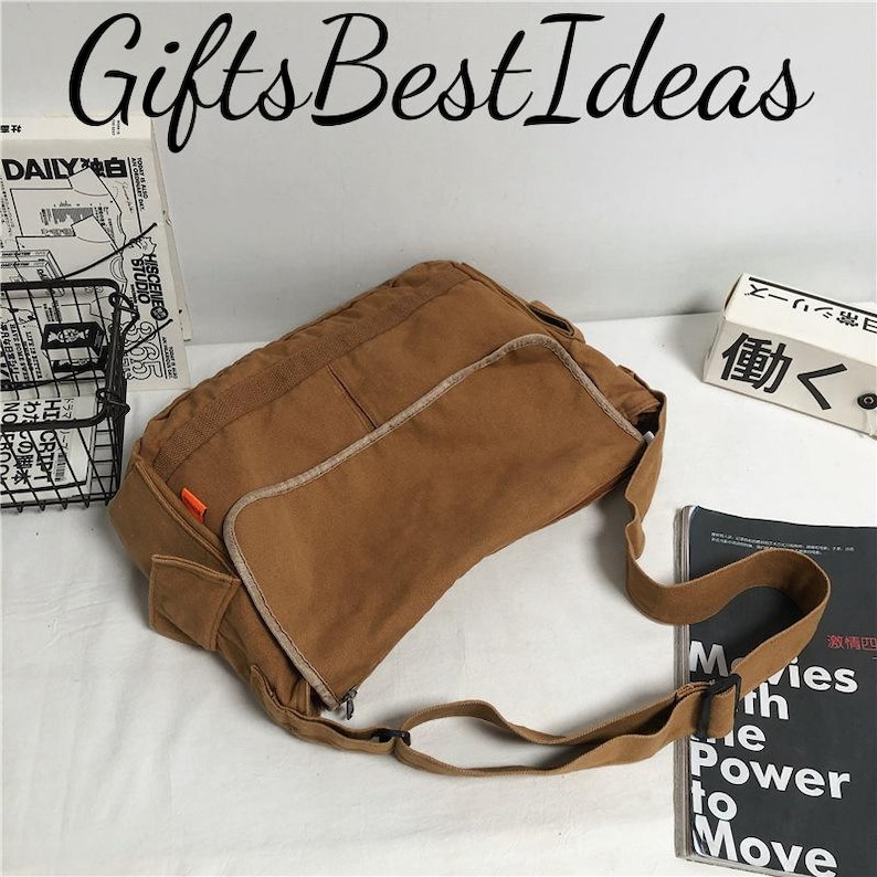 May include: A brown canvas messenger bag with an adjustable strap. The bag has a rectangular shape with a flap and pockets. The text "Gifts Best Ideas" is at the top. The bag is on a white surface.