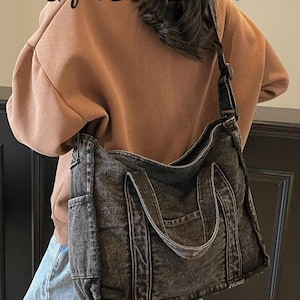 May include: A black denim tote bag with a shoulder strap and two handles. The bag has a pocket on the front and is worn over the shoulder. The text "Gifts Best Ideas" is visible in the image.
