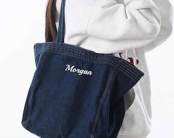 May include: A dark blue denim tote bag with the name "Morgan" in white script. The bag has a rectangular shape with a top handle and is being held by a person. The text "Gifts Best Ideas" is at the top.