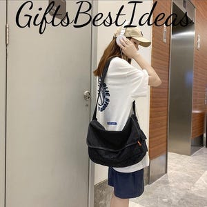 May include: A black messenger bag with a flap closure and an adjustable shoulder strap. The bag is worn over the shoulder. The image also shows a white t-shirt with blue text and a beige baseball cap. The text "Gifts Best Ideas" is at the top of the image.