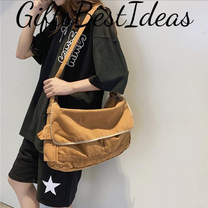 May include: A tan messenger bag with a large flap and a shoulder strap. The bag has a rectangular shape with a pocket on the front. The image also shows a black t-shirt and shorts with a white star.