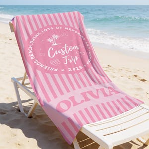 May include: Pink and white striped beach towel with the name "OLIVIA" in large letters. The towel has a circular design with the words "FRIENDS, BEACH, DRINK, LOTS OF MEMORIES AND LUGHTER" and the text "Custom Trip 2026".