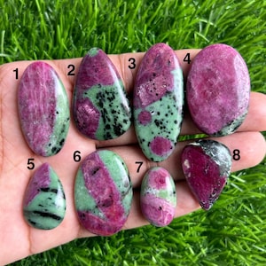 May include: A collection of eight polished ruby zoisite gemstones. The stones vary in shape and size, showcasing a mix of deep pink and green hues. Each stone has a unique pattern and texture, perfect for jewelry making or collecting.
