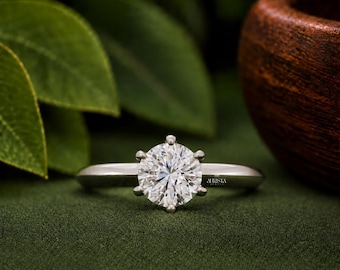 May include: A silver-toned ring featuring a single round-cut clear gemstone held in a six-prong setting. The band is smooth and polished, with the brand name Aurista engraved in small, clear lettering on the side of the metal shank.