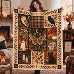 May include: A rectangular throw blanket featuring a central moth surrounded by panels of an owl, a crow, a ghost, a black cat, pumpkins, mushrooms, candles, and acorns. The design includes a plaid pattern and a border of leaves and berries.